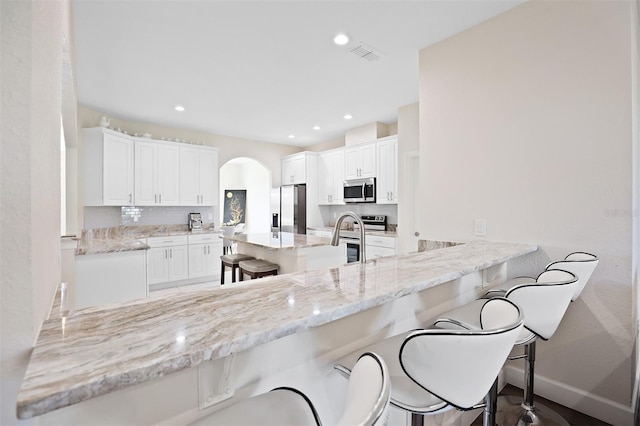 kitchen featuring kitchen peninsula, white cabinetry, stainless steel appliances, and a breakfast bar