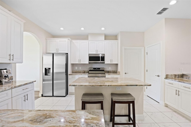 kitchen with white cabinetry, a center island, stainless steel appliances, light stone counters, and a breakfast bar