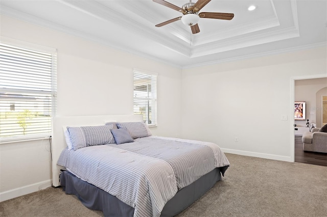 carpeted bedroom featuring ceiling fan, a raised ceiling, crown molding, and multiple windows