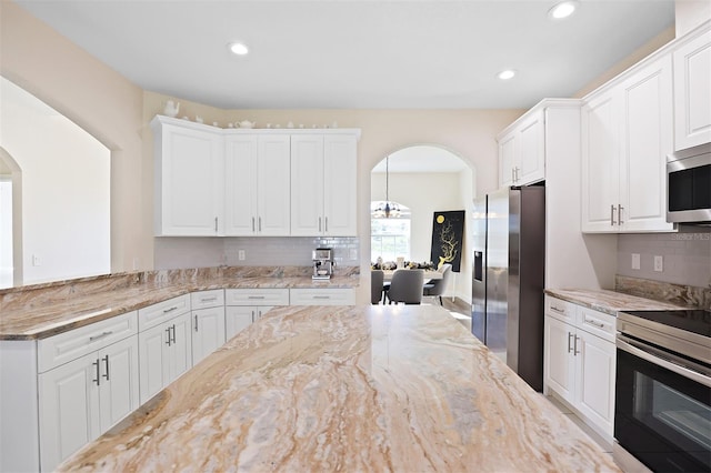 kitchen featuring pendant lighting, appliances with stainless steel finishes, tasteful backsplash, light stone counters, and white cabinetry