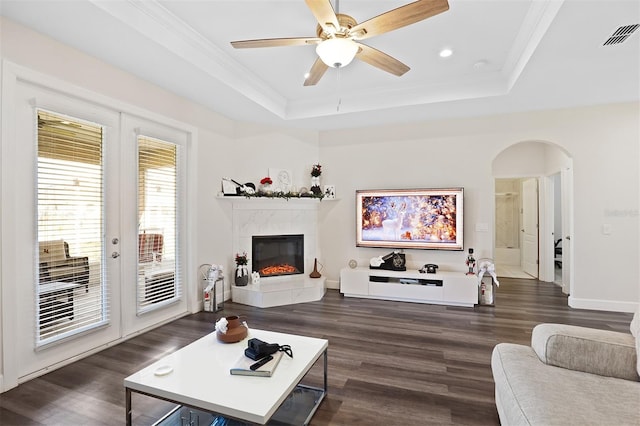 living room with ceiling fan, dark hardwood / wood-style floors, a tray ceiling, a tiled fireplace, and ornamental molding