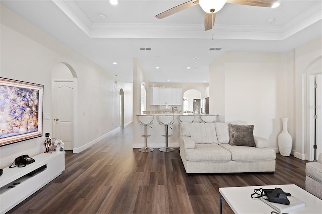 living room with dark hardwood / wood-style floors, ceiling fan, ornamental molding, and a tray ceiling