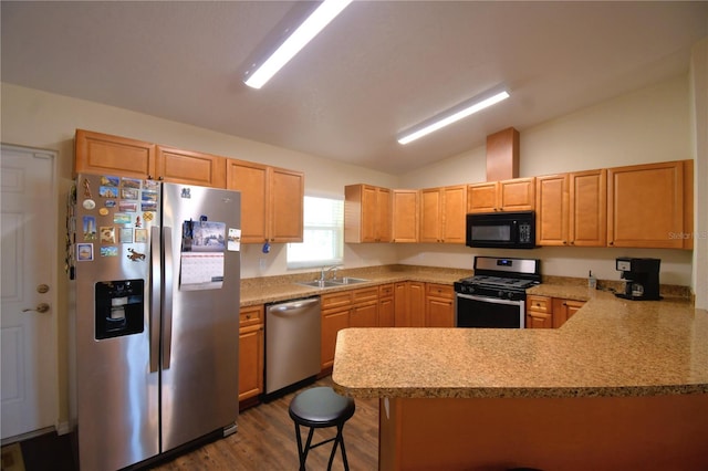 kitchen featuring a kitchen bar, vaulted ceiling, appliances with stainless steel finishes, dark hardwood / wood-style flooring, and kitchen peninsula