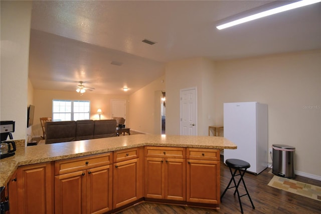 kitchen with kitchen peninsula, vaulted ceiling, ceiling fan, white refrigerator, and dark hardwood / wood-style floors