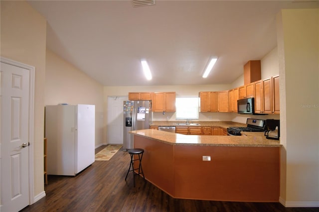 kitchen with appliances with stainless steel finishes, dark hardwood / wood-style flooring, vaulted ceiling, sink, and a breakfast bar area