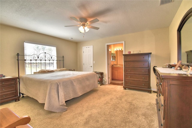 bedroom featuring a textured ceiling, light colored carpet, ensuite bath, and ceiling fan