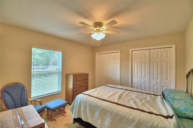 carpeted bedroom with ceiling fan, a textured ceiling, and multiple closets