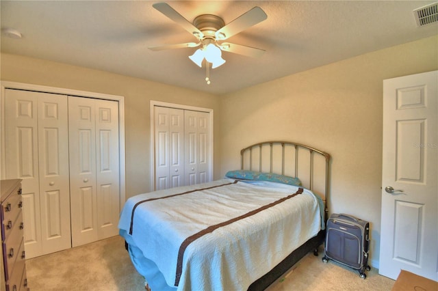 bedroom featuring multiple closets, ceiling fan, light colored carpet, and a textured ceiling