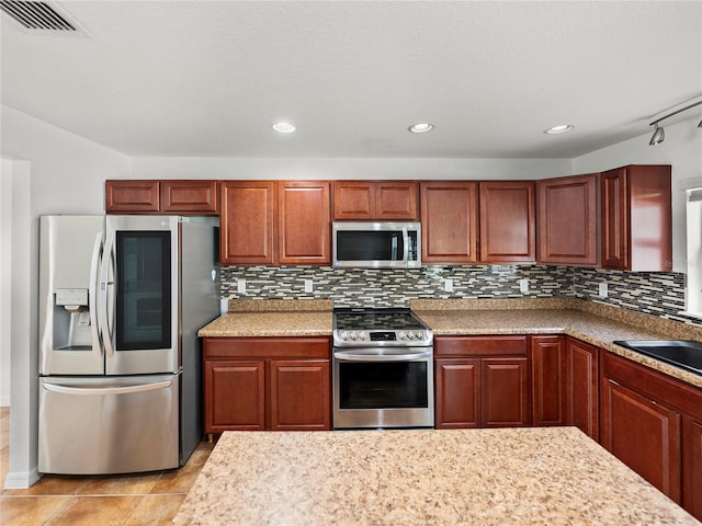 kitchen with appliances with stainless steel finishes, sink, light tile patterned floors, and decorative backsplash