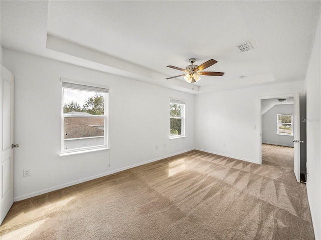 carpeted spare room with ceiling fan, a raised ceiling, and a healthy amount of sunlight