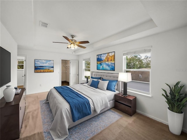 bedroom with ceiling fan, a raised ceiling, light carpet, and a spacious closet