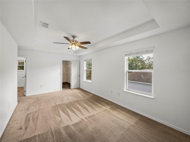 unfurnished bedroom featuring a tray ceiling, ceiling fan, light carpet, and a walk in closet