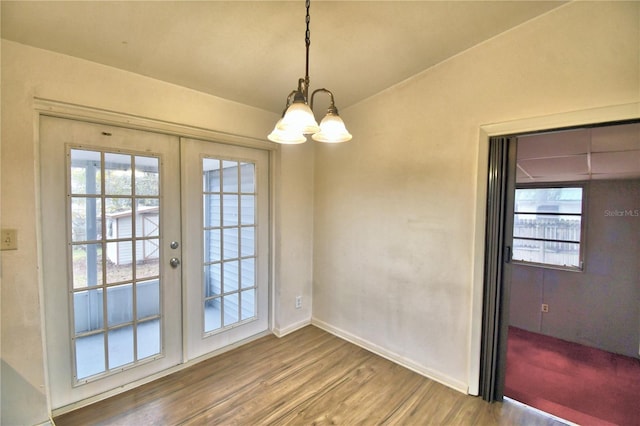 unfurnished dining area with french doors, an inviting chandelier, and wood-type flooring