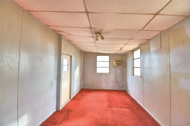 carpeted empty room with a wall mounted AC and a drop ceiling