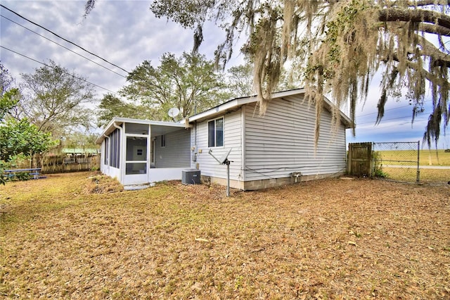 rear view of property featuring central AC unit, a sunroom, and a lawn