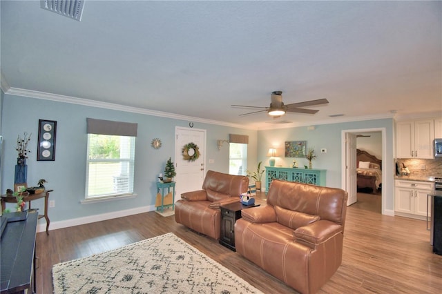 living room with crown molding, visible vents, a ceiling fan, light wood-type flooring, and baseboards