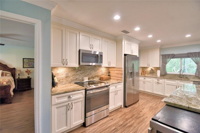 kitchen featuring ornamental molding, appliances with stainless steel finishes, light wood-type flooring, and white cabinets