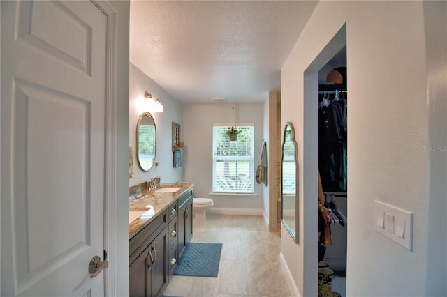 bathroom with a textured ceiling, toilet, a sink, a spacious closet, and double vanity