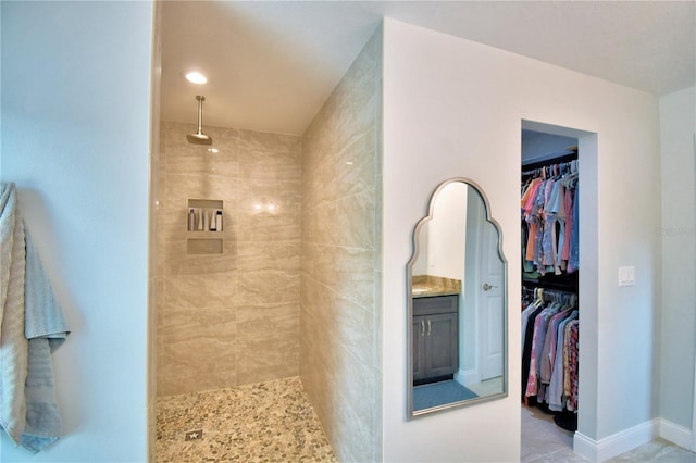 full bathroom with a walk in closet, tiled shower, and baseboards