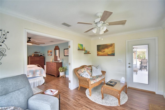 living area featuring wood finished floors, a ceiling fan, visible vents, baseboards, and ornamental molding