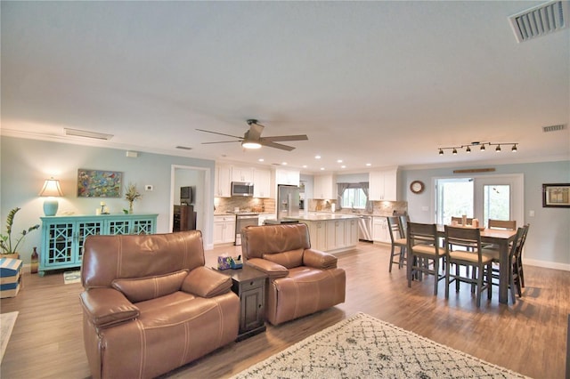 living room featuring ornamental molding, light wood-type flooring, visible vents, and baseboards