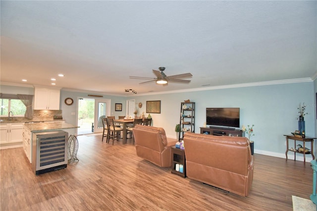 living area featuring recessed lighting, light wood-style floors, ornamental molding, beverage cooler, and baseboards