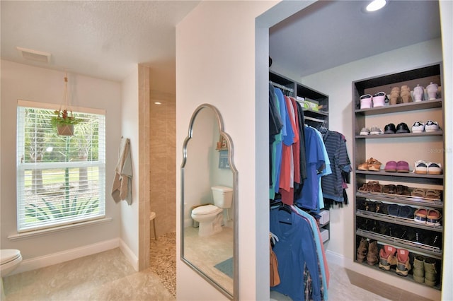 interior space with baseboards, toilet, a spacious closet, a textured ceiling, and a walk in shower