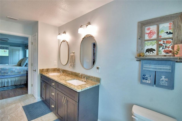 ensuite bathroom with double vanity, a sink, toilet, and connected bathroom