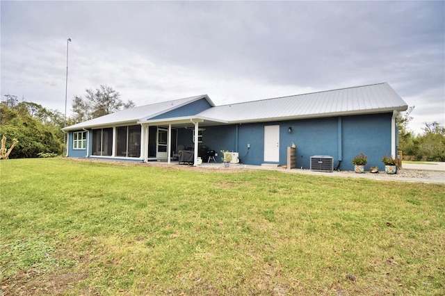 rear view of property with stucco siding, a lawn, a sunroom, central AC, and metal roof