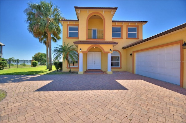 mediterranean / spanish-style home with a front lawn, a balcony, decorative driveway, and stucco siding