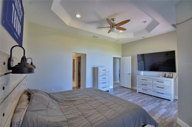 bedroom featuring a tray ceiling, wood finished floors, recessed lighting, a high ceiling, and baseboards