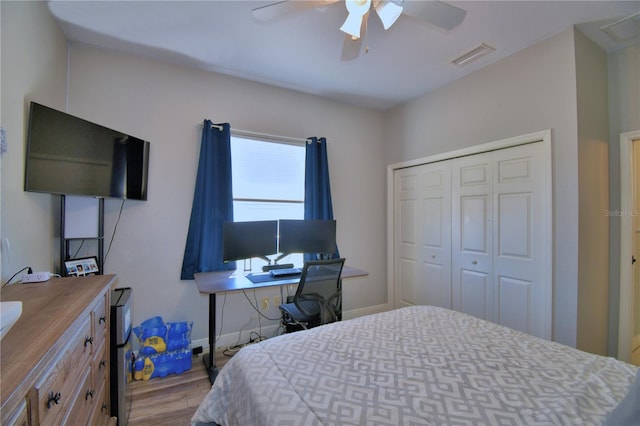 bedroom with wood finished floors, visible vents, baseboards, ceiling fan, and a closet