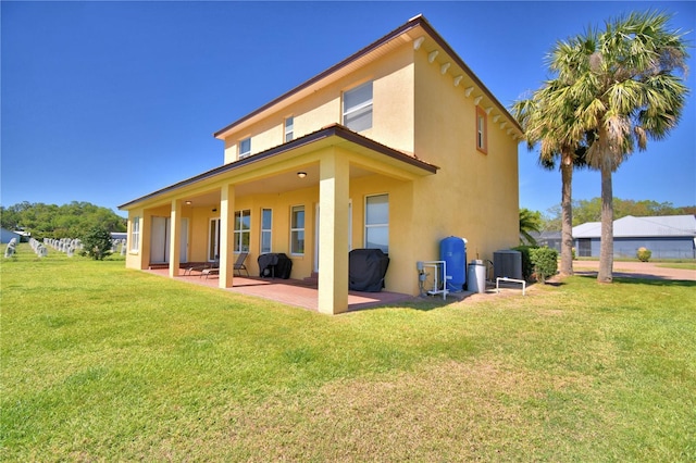 back of property with a patio area, stucco siding, a yard, and central AC