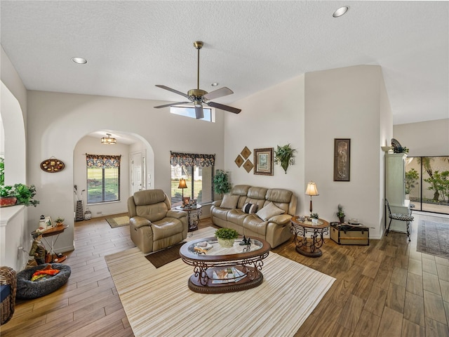 living room featuring ceiling fan, hardwood / wood-style floors, a textured ceiling, and a towering ceiling