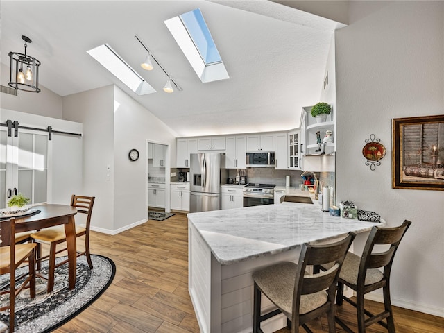 kitchen featuring light hardwood / wood-style flooring, appliances with stainless steel finishes, light stone countertops, decorative light fixtures, and kitchen peninsula