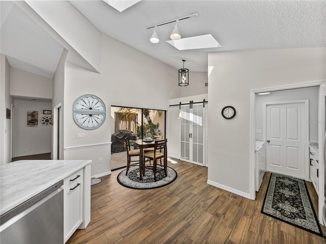 foyer entrance with dark wood-type flooring, vaulted ceiling with skylight, a textured ceiling, track lighting, and a barn door