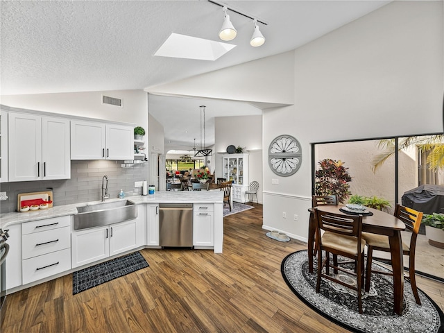 kitchen featuring lofted ceiling with skylight, sink, decorative light fixtures, dishwasher, and white cabinets