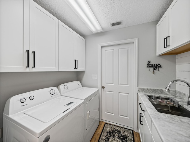 laundry area featuring sink, cabinets, a textured ceiling, hardwood / wood-style flooring, and washing machine and dryer