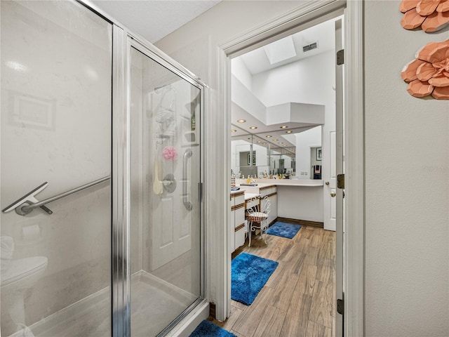 bathroom with hardwood / wood-style flooring, vanity, a skylight, and a shower with door