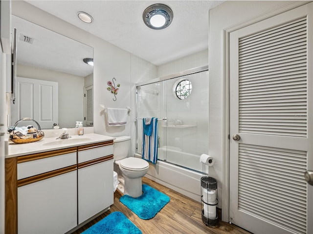 full bathroom with bath / shower combo with glass door, hardwood / wood-style flooring, vanity, toilet, and a textured ceiling