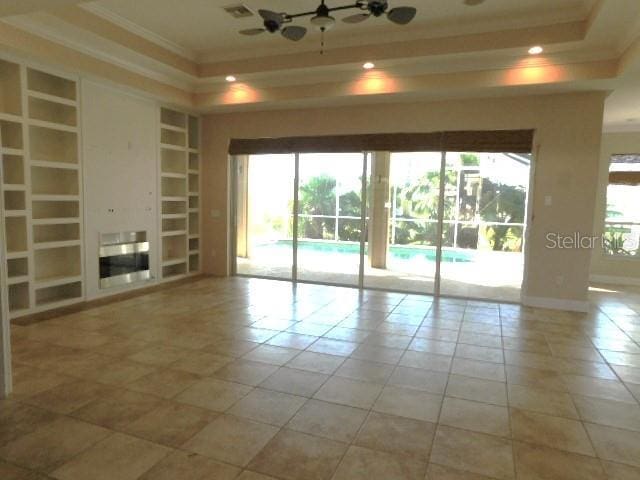 unfurnished room featuring built in shelves, ornamental molding, a healthy amount of sunlight, and a tray ceiling