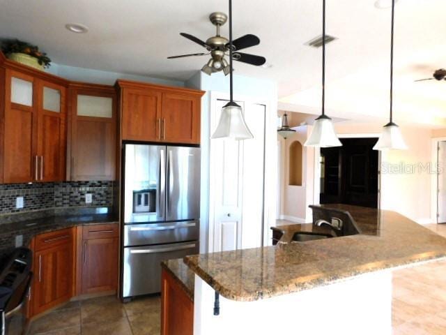 kitchen featuring stainless steel refrigerator with ice dispenser, decorative light fixtures, ceiling fan, gas range oven, and decorative backsplash