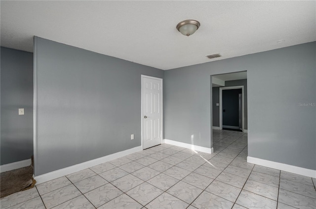 unfurnished room with a textured ceiling, visible vents, marble finish floor, and baseboards