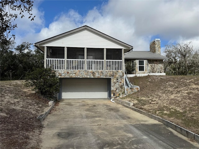 view of front of house featuring stone siding, a chimney, an attached garage, and driveway