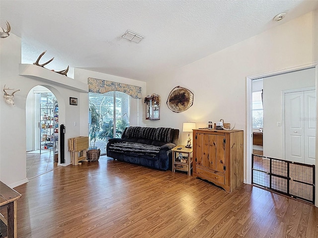 living area with arched walkways, visible vents, wood finished floors, and a textured ceiling