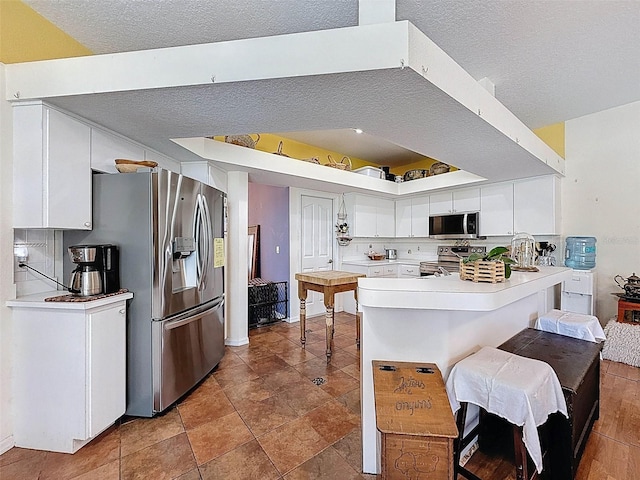 kitchen featuring a peninsula, stainless steel appliances, light countertops, white cabinetry, and a textured ceiling