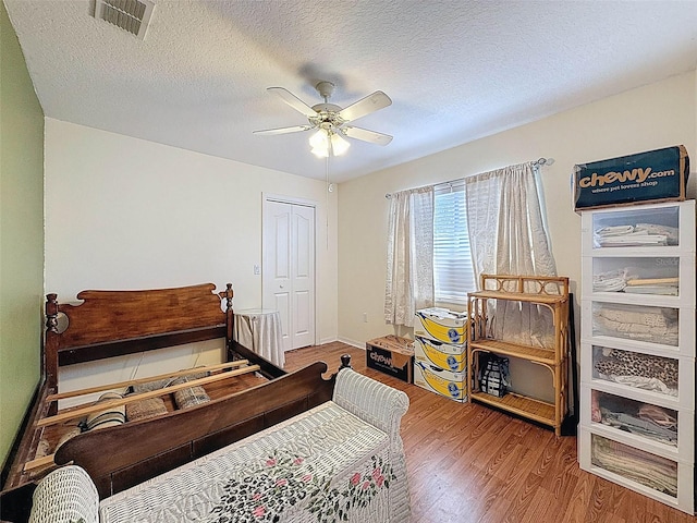 bedroom with wood finished floors, a closet, visible vents, a ceiling fan, and a textured ceiling