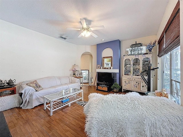 living area with visible vents, arched walkways, ceiling fan, and wood finished floors