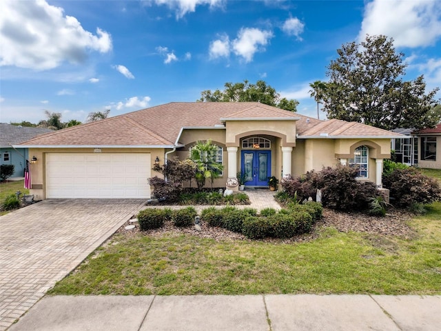 view of front of property featuring stucco siding, decorative driveway, french doors, a front lawn, and an attached garage