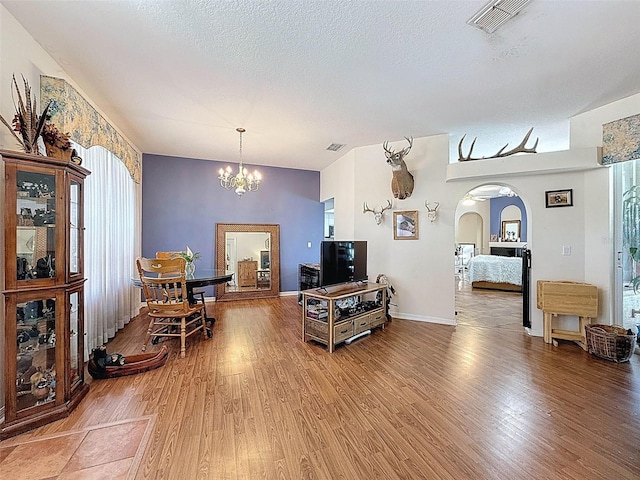 living area featuring visible vents, a chandelier, light wood finished floors, and arched walkways